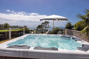Un bain à remous à bords ondulés, entouré d’une clôture en verre, offrant une vue sur l’océan et un ciel dégagé.