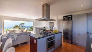 Une cuisine moderne dotée d’un îlot central, d’appareils électroménagers en acier inoxydable et offrant une vue sur l’extérieur.