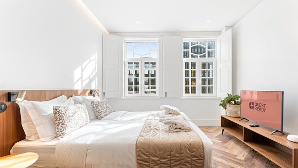 A modern hotel room with a large bed, two windows, a TV, and a wooden floor. - GuestReady - Santa Barbara Garden House 13 (Braga)