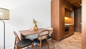 A dining area with a wooden table, two chairs, a vase with flowers, and a modern kitchen in the background. - GuestReady - Santa Barbara Garden House 13 (Braga)