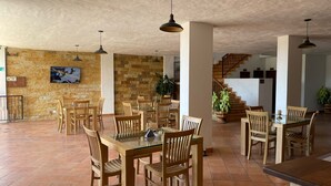Un'ampia sala da pranzo con tavoli e sedie in legno, un muro in pietra e una scala che conduce al piano superiore.