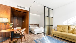 A modern hotel room with a wooden desk, a bed, a sofa, and a glass partition. - GuestReady - Santa Barbara Garden House 12 (Braga)