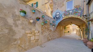 A narrow cobblestone street with a stone wall, potted plants, and a mural. - VISTA SU MONTECRISTO - VISTA SU MONTECRISTO (Capoliveri)