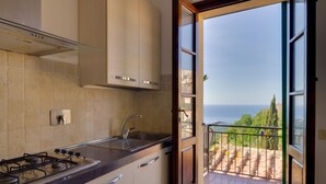 A kitchen with a gas stove, a sink, and cabinets. There's a balcony with a view of the sea. - VISTA SU MONTECRISTO - VISTA SU MONTECRISTO (Capoliveri)