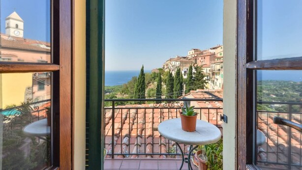 A balcony with a view of a coastal town, a small table, and potted plants. - VISTA SU MONTECRISTO - VISTA SU MONTECRISTO (Capoliveri)