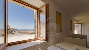 Ein Zimmer mit großem Fenster, einem Tisch mit Papieren und Blick auf eine Küstenlandschaft.
