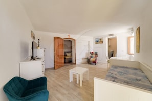 A spacious living room with a teal armchair, a white coffee table, a wooden door leading to another room, and a colorful armchair.