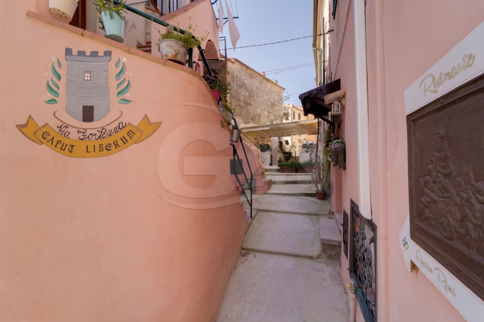 A narrow alleyway with a pink building on the left, a castle-like emblem, and a sign reading 'Caput Liburnum.'