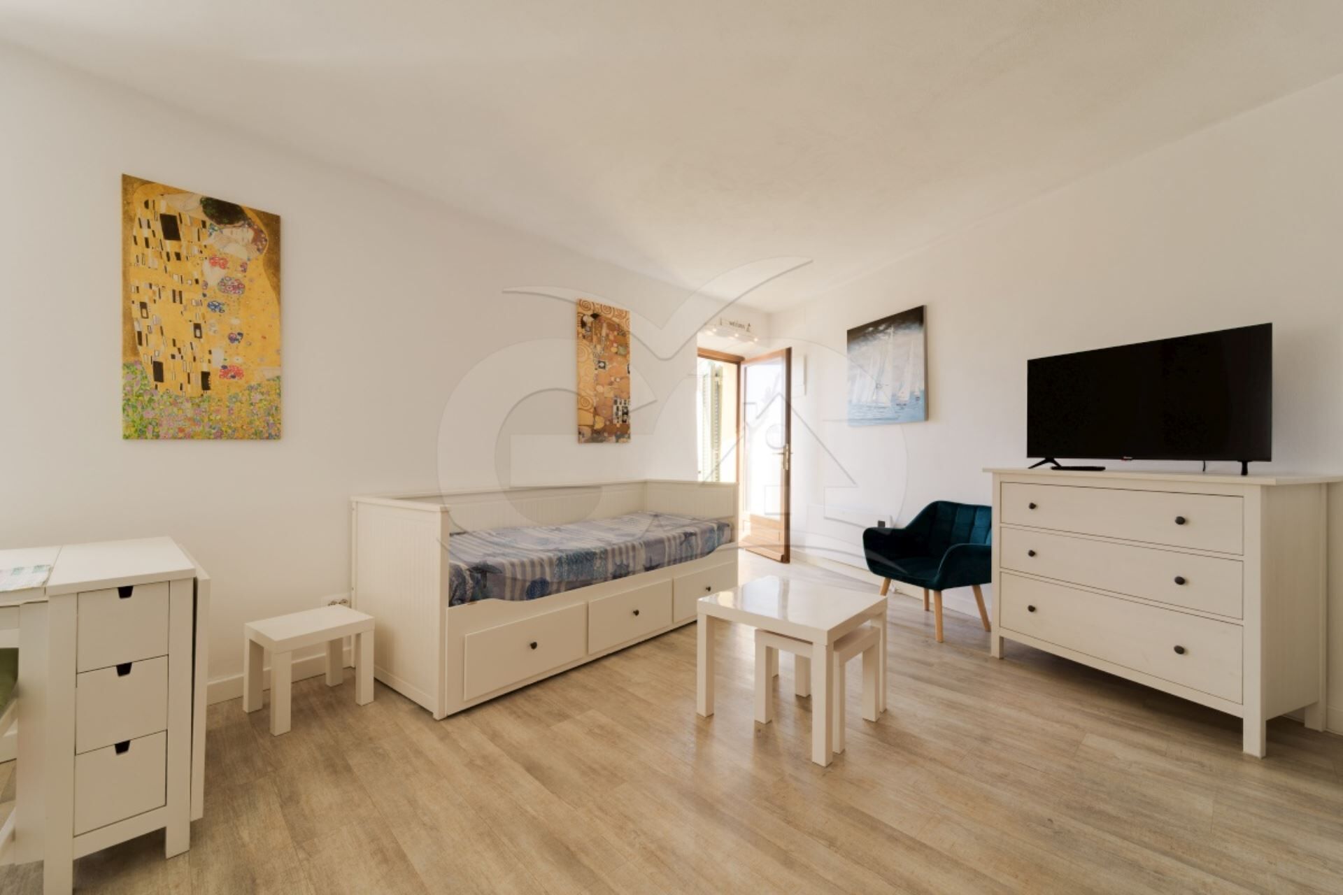 Een moderne, goed verlichte kamer met een bed, een bureau, een televisie en kunstwerken aan de wanden.