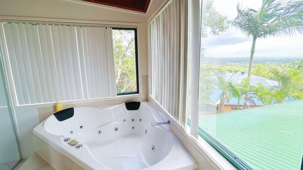Un baño con bañera, una ventana con persianas y vistas a la vegetación.