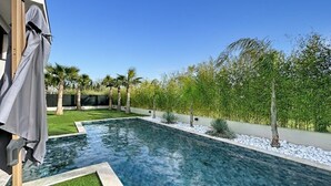 A swimming pool with clear water, surrounded by a landscaped garden with palm trees and shrubs. - Luxury Villa in Grimaud (GRIMAUD)