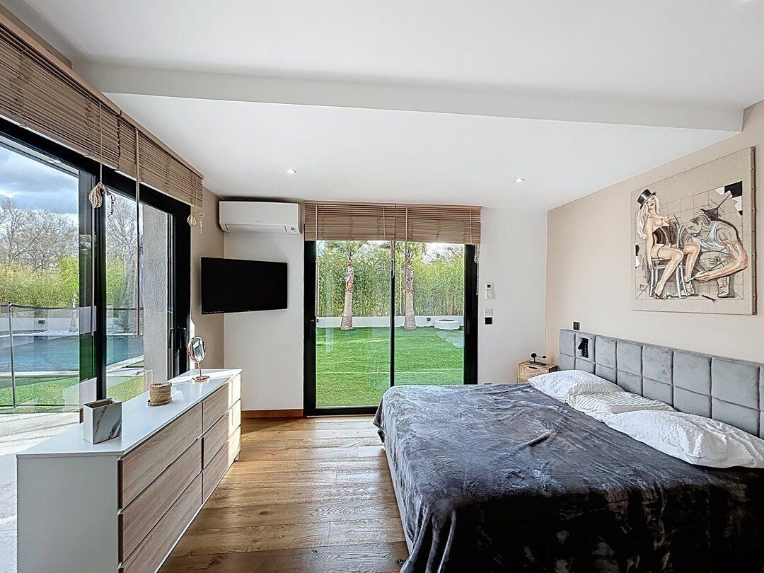 Een slaapkamer met een bed, een dressoir, een televisie en een groot raam met uitzicht op een tuin.
