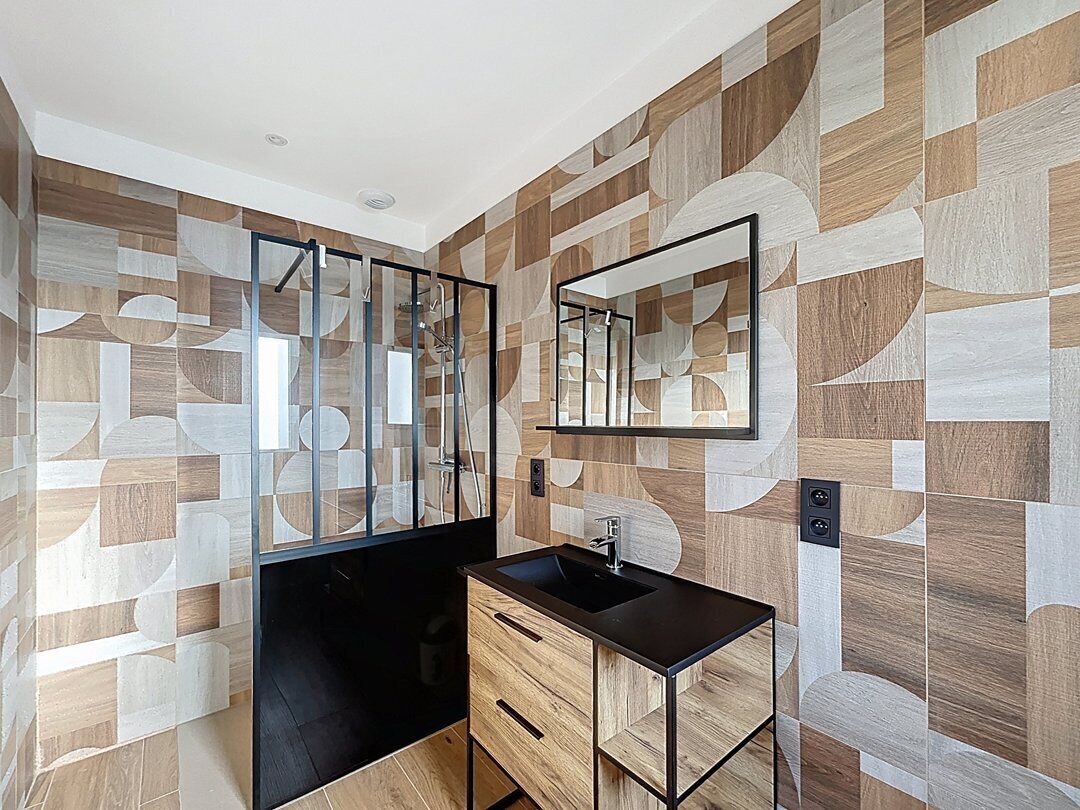 Un baño con pared de diseño geométrico, un lavabo negro y un espejo.