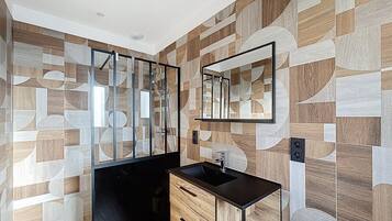 Un baño con pared de diseño geométrico, un lavabo negro y un espejo.