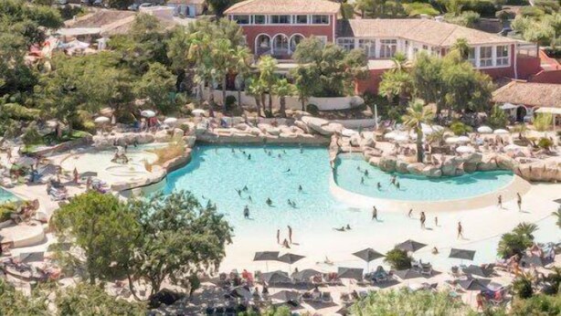En semesteranläggning vid kusten med flera byggnader, ett centralt poolområde och omgivande grönska.