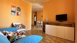 Sala de estar com sofá, televisão e área de jantar com cadeiras.