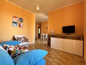 A living room with a sofa, a TV, and a dining area with chairs. - Capo d'Arco - Agrumeto (Rio Marina)