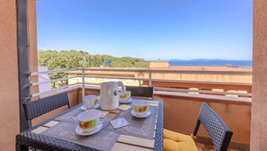 Ein Balkon mit Tisch für zwei Personen, einem Wasserkocher und zwei Tassen. Im Hintergrund ist ein Gewässer und ein bewaldeter Hügel zu sehen.