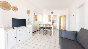 Ein modernes, helles Wohnzimmer mit einem Flachbildfernseher, einer Couch und einem Essbereich mit Stühlen.