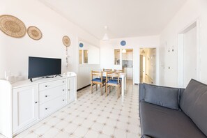 Ett modernt och väl upplyst vardagsrum med en platt-TV, en soffa och en matplats med stolar.