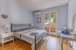 A bedroom with a bed, bedside tables, a desk, and a window with a view of greenery.
