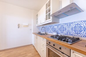 A kitchen with white cabinets, a wooden countertop, a gas stove, and blue patterned backsplash.