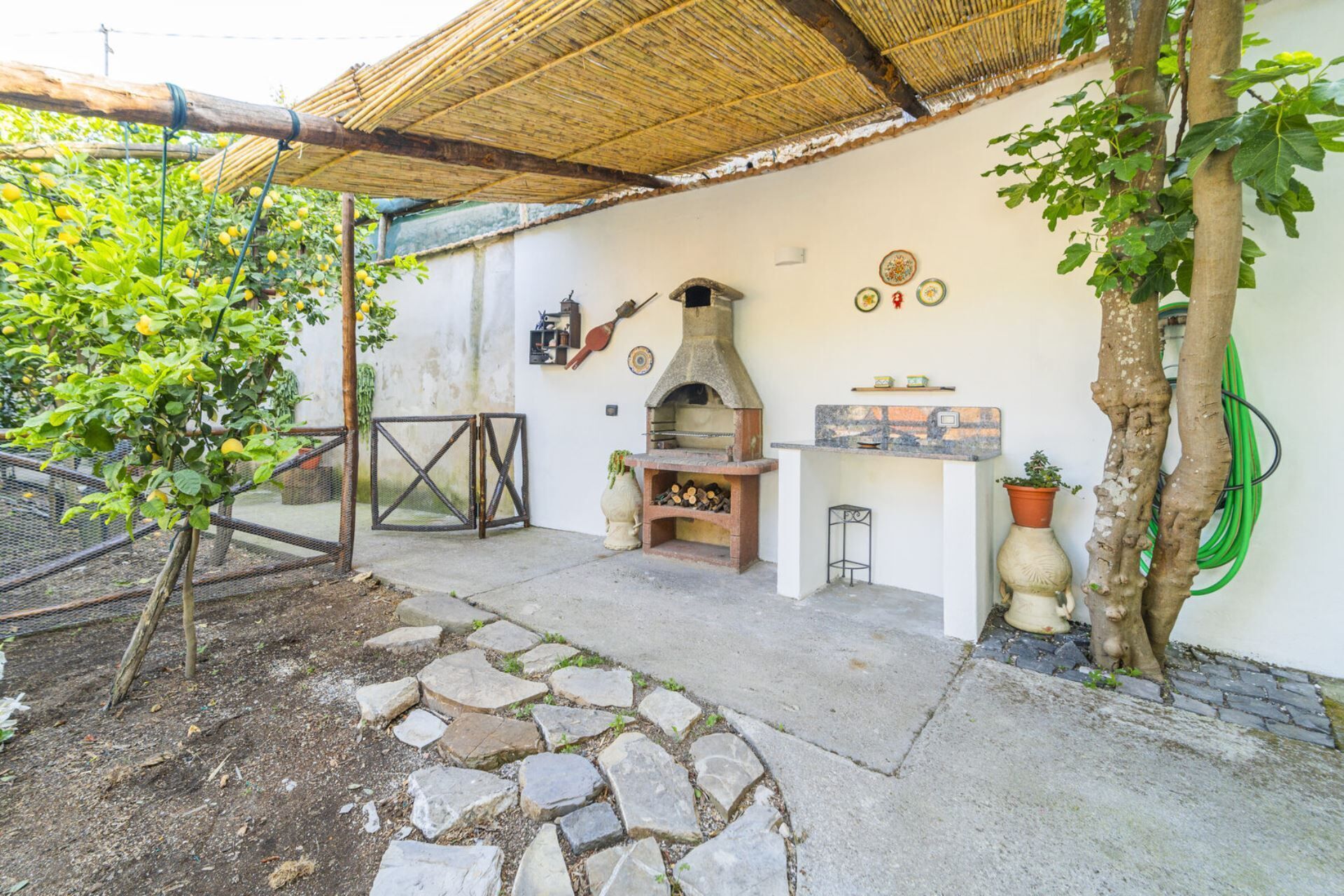 Ein rustikaler Außenbereich mit einer Steinstraße, einer Holzpergola und einem Backofen aus Ziegeln.