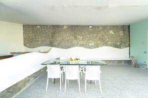A dining area with a glass table and white chairs, a stone wall, and a tiled floor. - Atelier sul Mare exclusive property near the sea in Minori, Amalfi Coast (Minori)