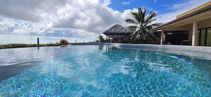 A clear swimming pool with a tiled edge, a thatched-roof structure, and a palm tree. - Villa with Pool & Jacuzzi, 180° panoramic view of the sea and Moorea (Punaauia)