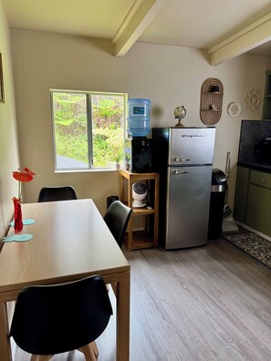 A compact kitchen with a refrigerator, water dispenser, and a small dining table with chairs. - Rainforest Studio in Volcano- 3miles from National Park (Volcano)