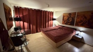 A bedroom with a bed, a desk, a chair, a lamp, and curtains. - Centurio 5 :Double room with balcony (Augst)