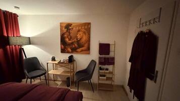 Habitación de hotel con una cama, dos sillas, un escritorio, un cuadro, un armario y un perchero.