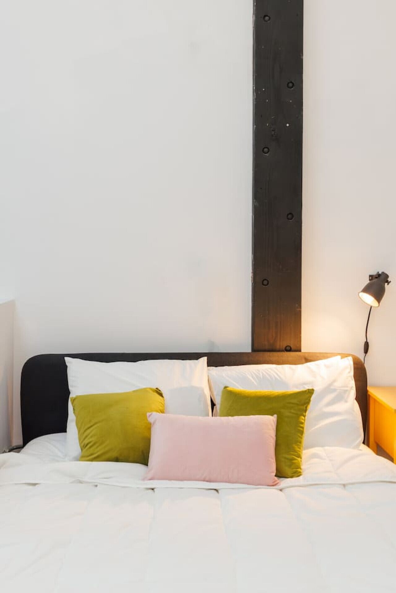 A bed with white bedding and multiple pillows in various colors, a dark headboard, and a bedside lamp.