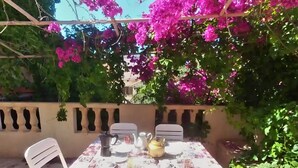 Un patio al aire libre con una mesa lista para dos personas, rodeado de follaje exuberante y flores rosas vibrantes.