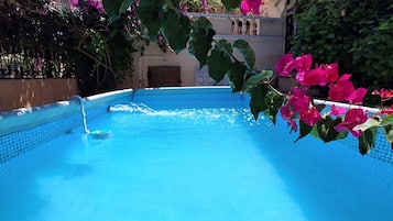Una piscina con agua azul cristalina, rodeada de exuberante vegetación y flores rosadas.