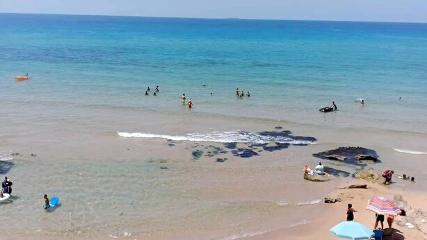 Una playa con agua cristalina, gente nadando y algunas sombrillas.