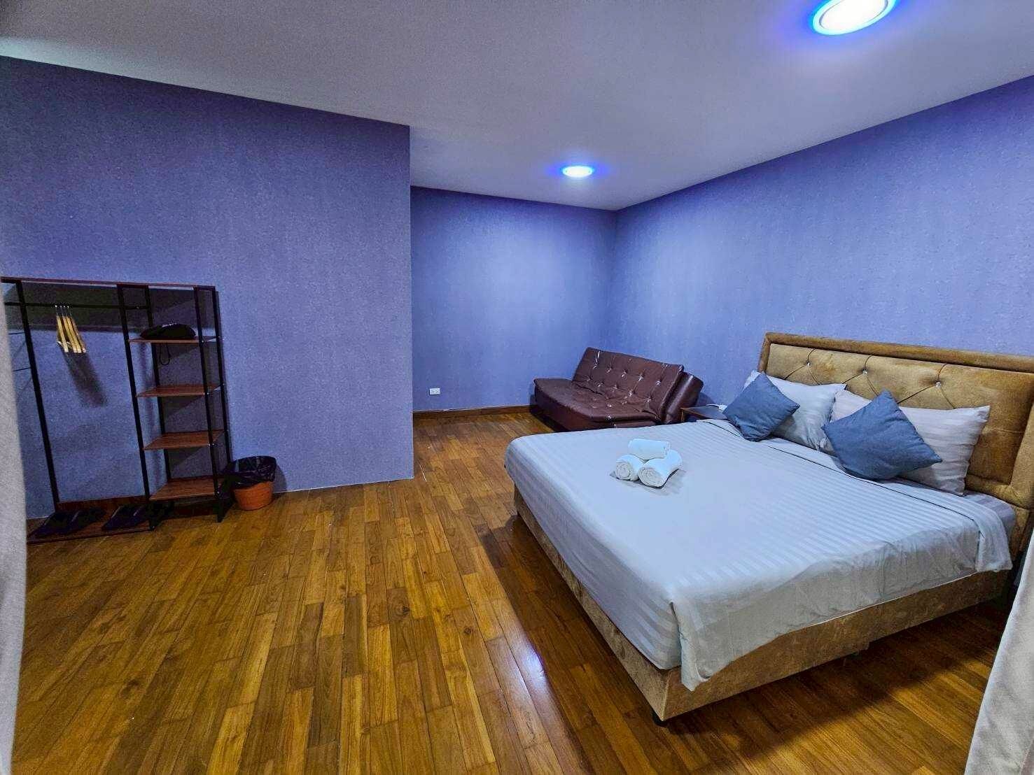 A bedroom with a bed, a wardrobe, a brown leather sofa, and a wooden floor.