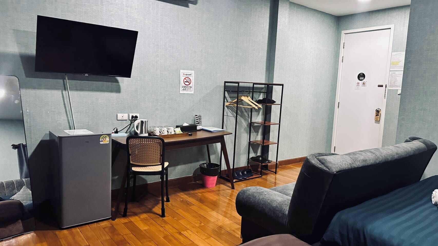 Quarto pequeno com escrivaninha, cadeira, televisão e sofá.