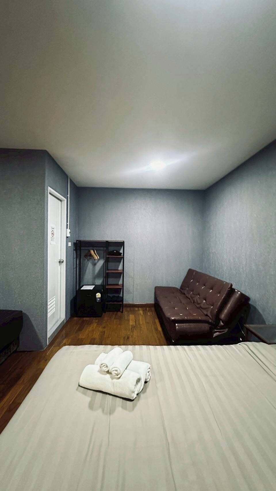 A bedroom with a bed, a brown leather sofa, a wardrobe, and a wooden floor.
