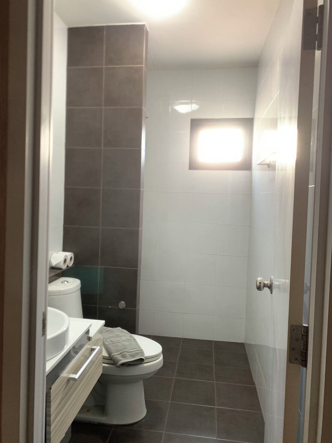 Un baño pequeño y moderno con inodoro, lavamanos y zona de ducha.
