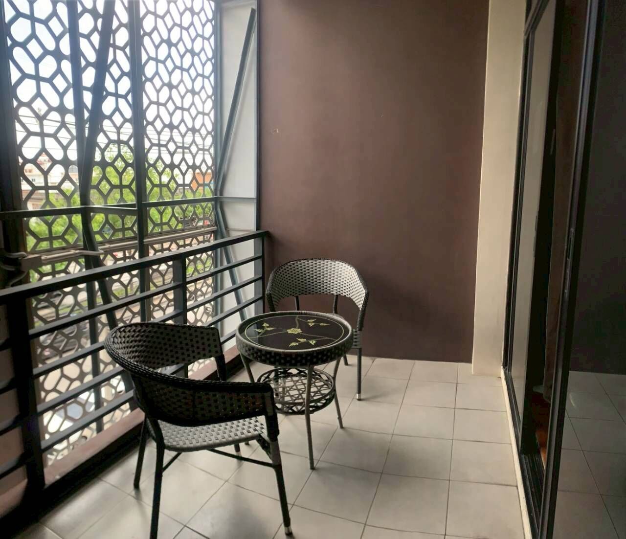 A balcony with two chairs and a small round table, a metal railing, and a view of greenery outside.
