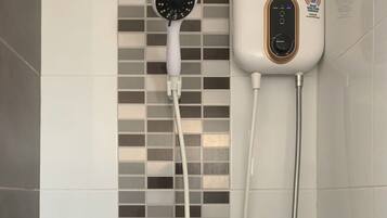 A shower with a handheld showerhead, a wall-mounted control panel, and three black bottles with pumps on a tiled wall.