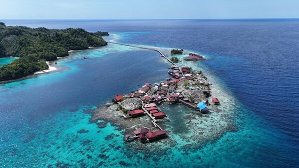 An aerial view of a coastal property with multiple buildings, a pier, and clear turquoise waters.