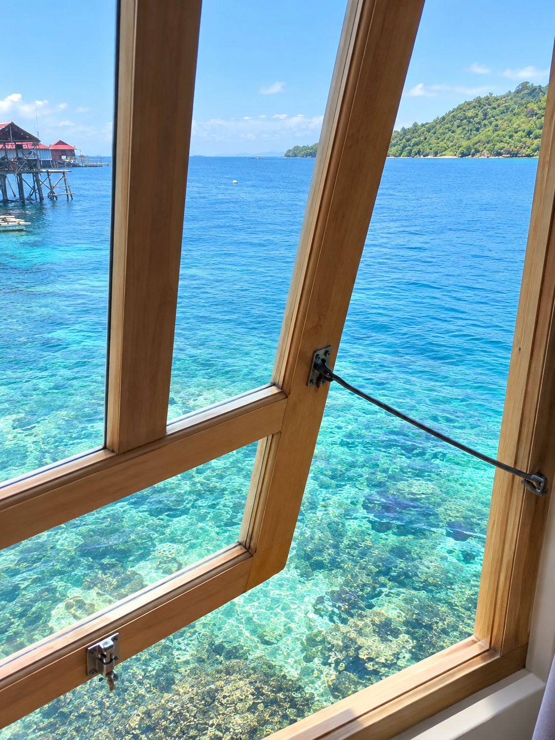 A window with a view of clear blue water and a distant island.