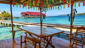 Un pontile in legno con tavoli da picnic che si affaccia su acque turchesi e un molo con bungalow sull'acqua.