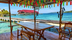 A wooden deck with picnic tables overlooking turquoise water and a pier with overwater bungalows. - Nur Homestay Mini Resto and Souvenir (Papan Island)