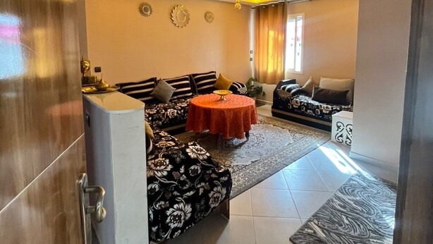 A living room with a sofa, a dining table, and a kitchen area.