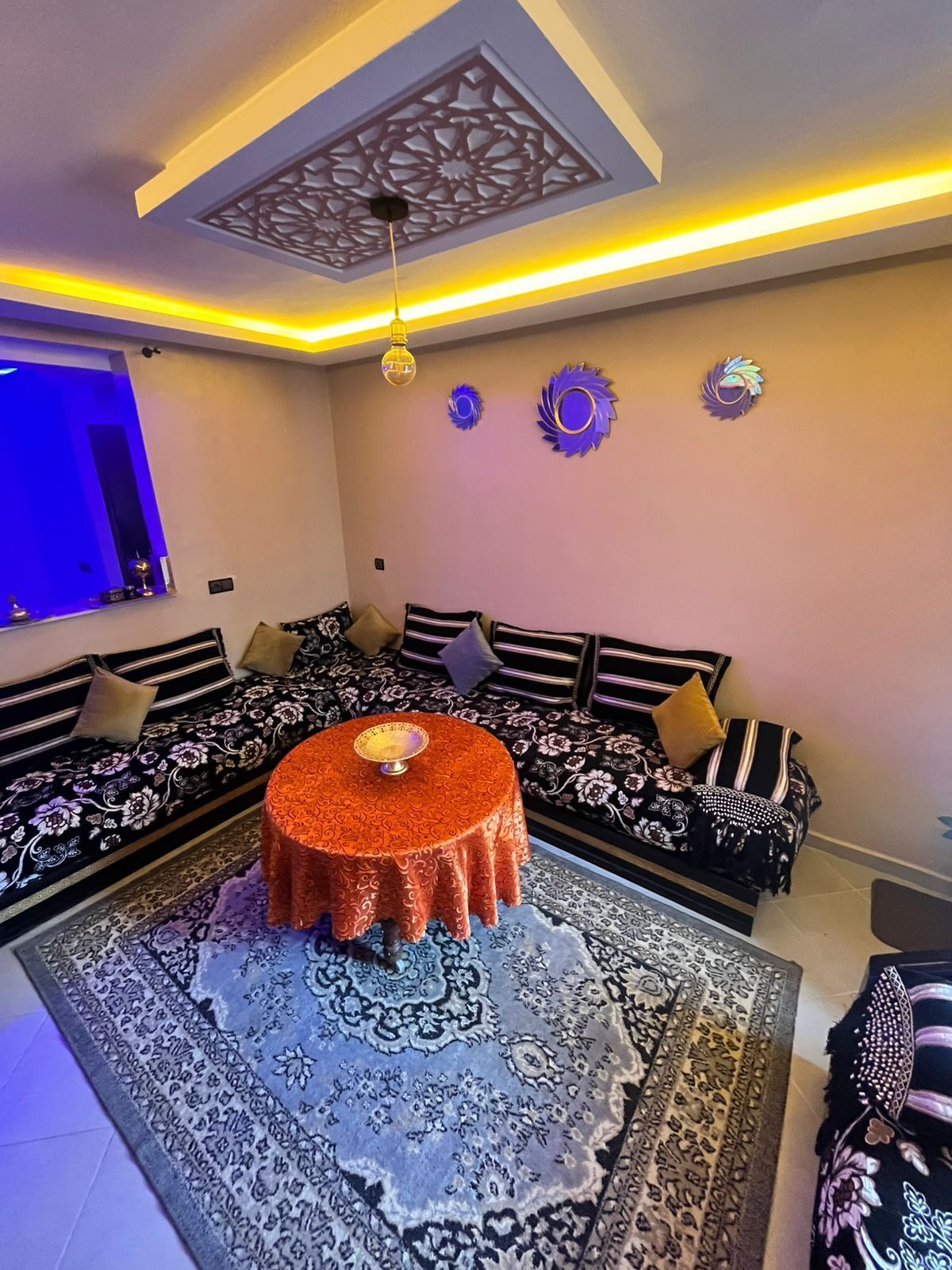 A modern living room with a sofa set, a round coffee table, decorative wall art, and a ceiling light fixture.