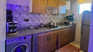 A compact kitchen with a washing machine, wooden cabinets, patterned tiles, and a built-in oven.