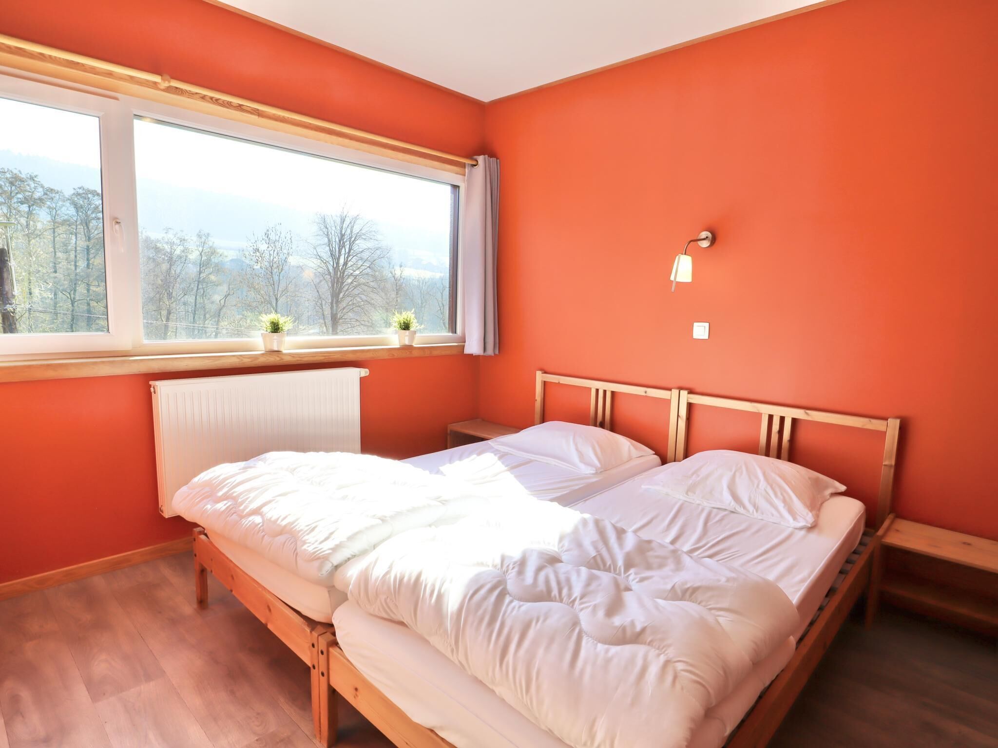 Une chambre à coucher avec un lit en bois, une fenêtre donnant sur des arbres et un radiateur.